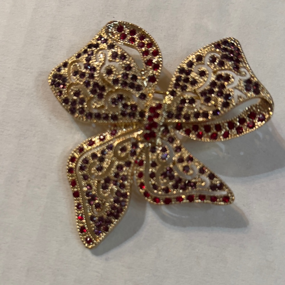 Brooch gold toned bow with red and purple rhinestones.